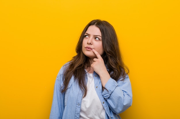 Young curvy plus size woman looking sideways with doubtful and skeptical expression.