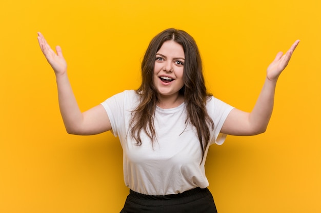 Young curvy plus size woman receiving a pleasant surprise, excited and raising hands.