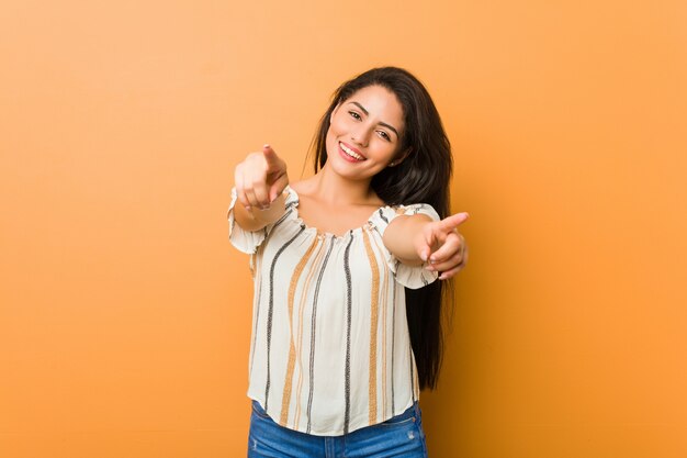 Young curvy woman cheerful smiles pointing to front