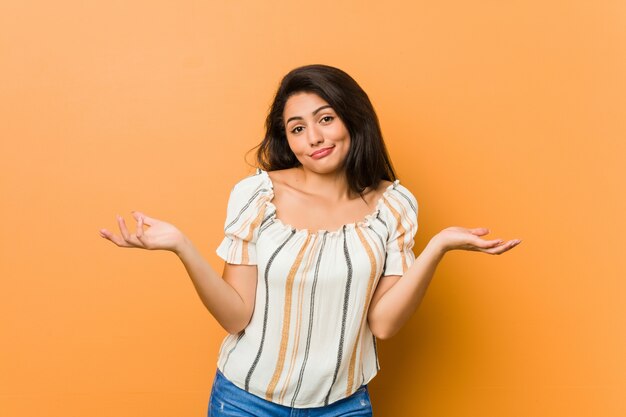 Young curvy woman doubting and shrugging shoulders in questioning gesture.