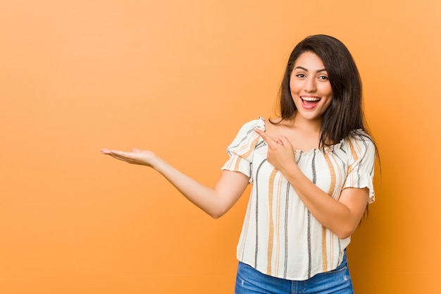 Young curvy woman excited holding a copy space on palm.