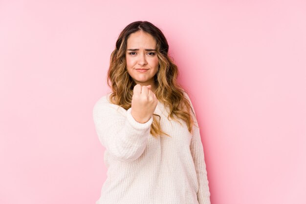 Young curvy woman posing in a pink wall isolated showing fist with aggressive facial expression.