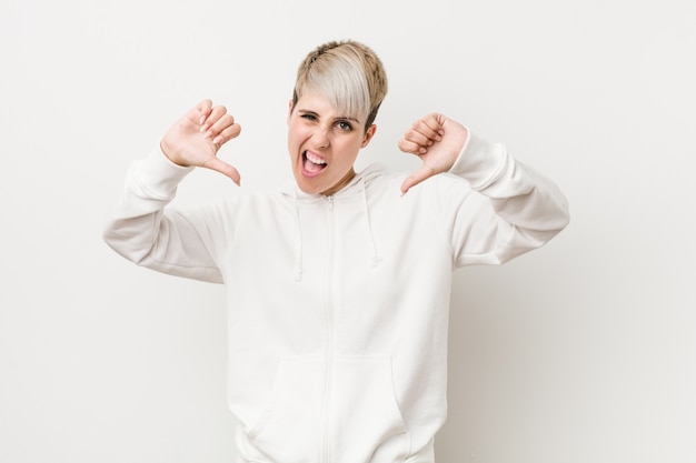 Young curvy woman wearing a white hoodie showing thumb down and expressing dislike.