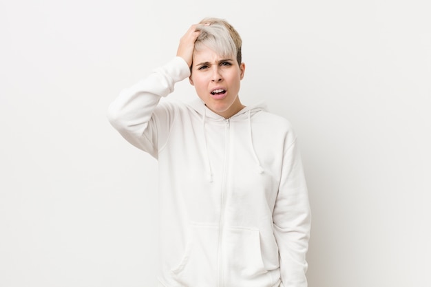 Young curvy woman wearing a white hoodie tired and very sleepy keeping hand on head.