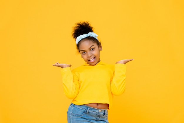 Young cute African American mixed race girl smiling and doing open palms gesture isolated on colorful yellow wall