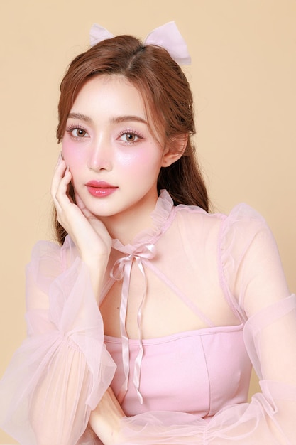 Young cute Asian woman in a pink elegant dress Korean style makeup moisturized smooth perfect skin on a beige background Facial treatment Cosmetology plastic surgery