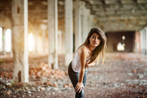 Young cute brunette girl wearing on black leather pants and white blouse posed on abandoned place.