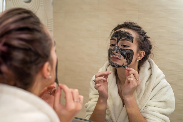 Young cute brunette makes a gorgeous clay black mask from pimples and blackheads