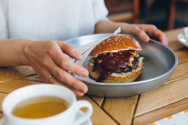 Young cute brunette woman eating a freshly prepared delicious Burger in the cafe. Toning.