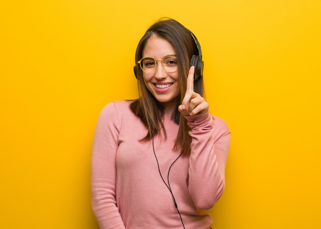 Young cute woman listening to music showing number one