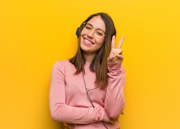 Young cute woman listening to music showing number two