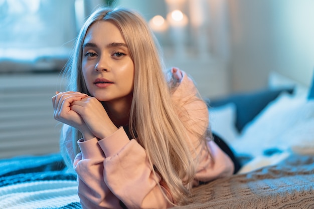 Young Cute Woman Lying Down On A Bed With Pillows Looking At Camera Touching Face With Hands