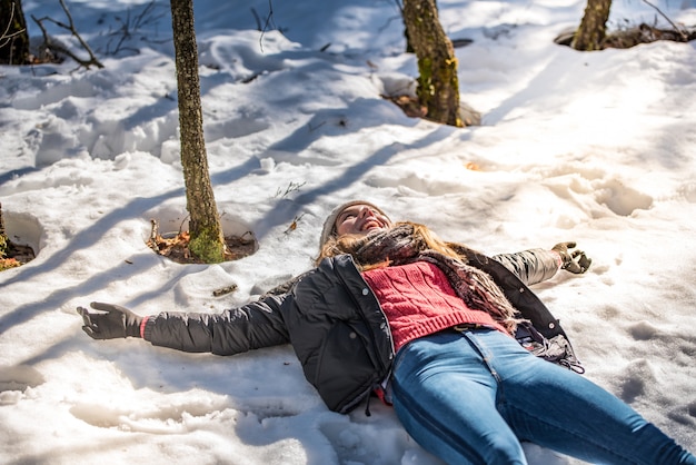 Young cute woman lying playing and enjoying snow in winter