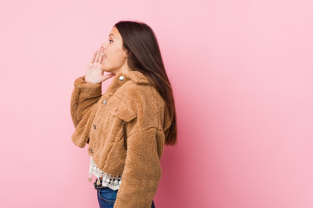 Young cute woman shouting and holding palm near opened mouth.