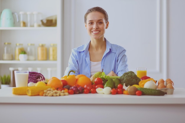 Young and cute woman sitting at the table full of fruits and vegetables in the wooden interior