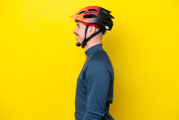 Young cyclist caucasian man isolated on yellow background laughing in lateral position