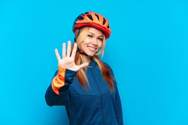 Young cyclist girl isolated on blue background counting five with fingers