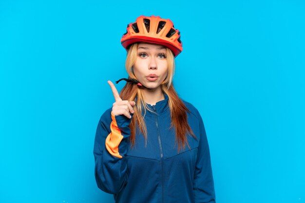 Young cyclist girl isolated on blue background intending to realizes the solution while lifting a finger up