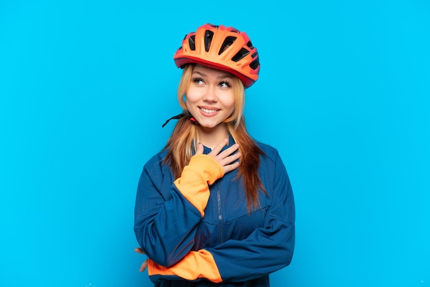 Young cyclist girl isolated on blue background looking up while smiling