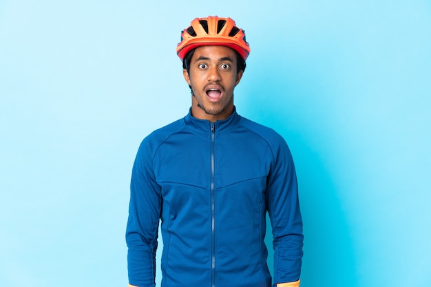 Young cyclist man with braids over isolated wall with surprise facial expression