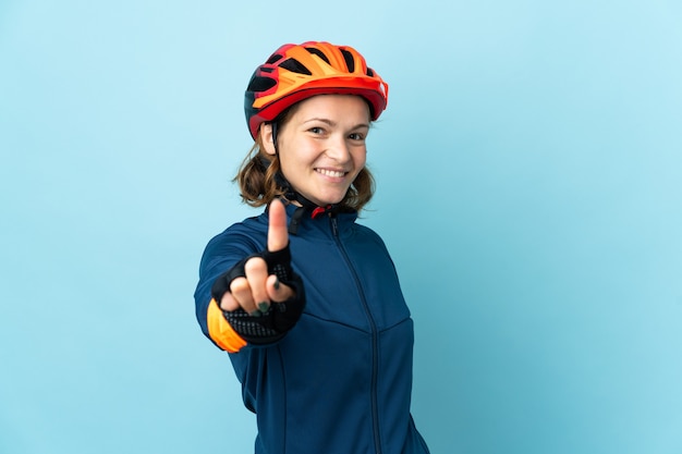 Young cyclist woman isolated on blue wall showing and lifting a finger