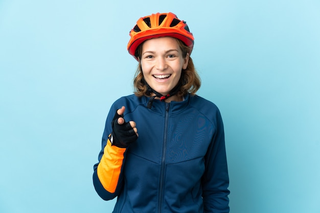 Young cyclist woman isolated on blue wall surprised and pointing front