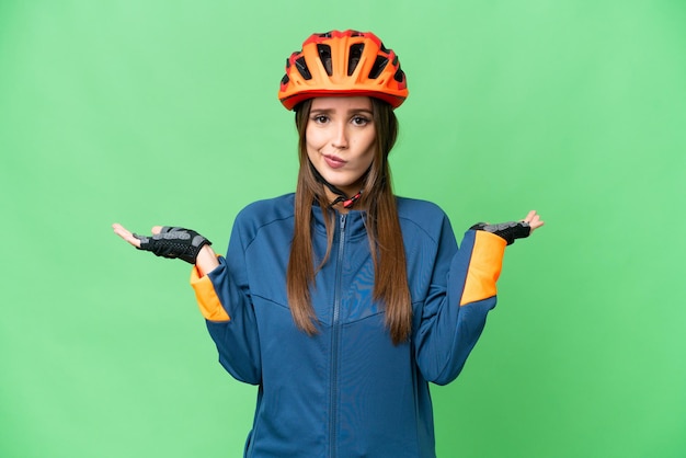 Young cyclist woman over isolated chroma key background having doubts while raising hands