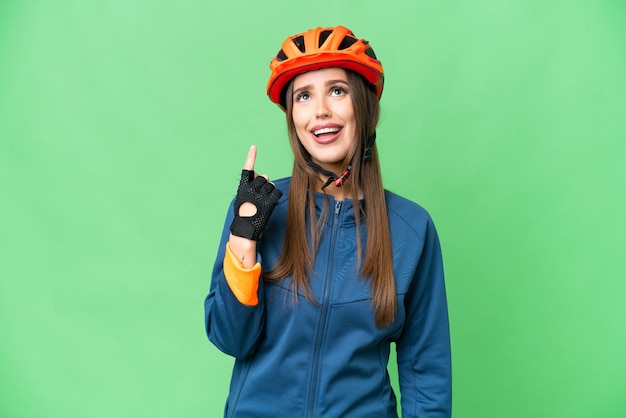 Young cyclist woman over isolated chroma key background pointing up and surprised