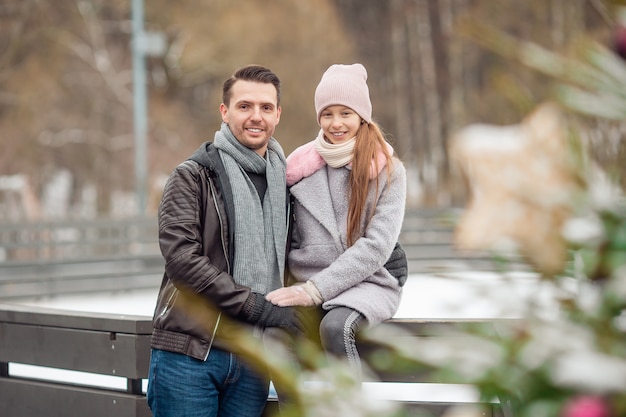 Young dad and adorable little girl have fun on skating rink outdoors