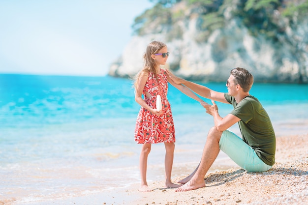 Young dad applying sun cream to daughter nose on the beach. Sun protection