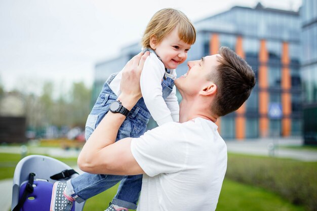 A young dad sits a small daughter in a chair before riding a bicycle.