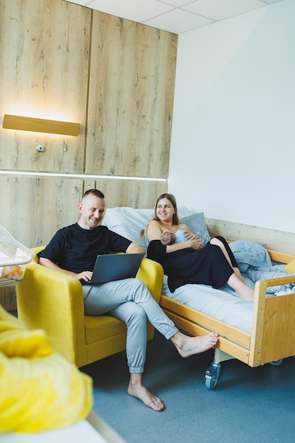 Young dad works online on a laptop while his wife plays with the baby Young happy modern couple