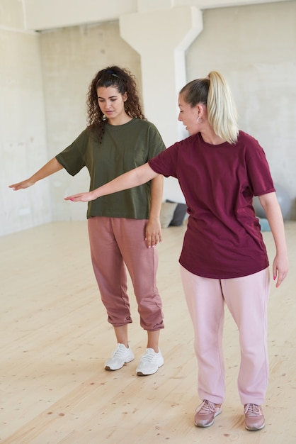 Young dance instructor showing the movement to woman and teaching her to dance in studio