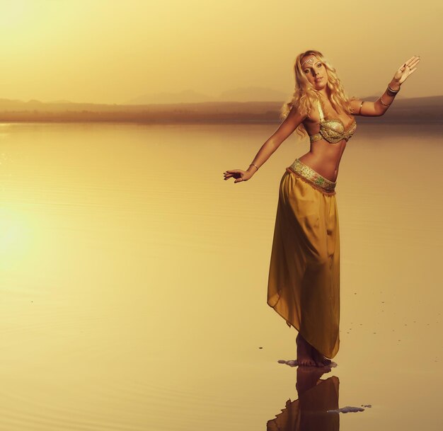 Photo young dancer posing on sea shore against clear sky during sunset