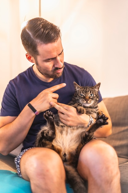 A young dark-haired Caucasian in a blue shirt with his lovely gray and white domestic cat. The cat man's best friend. Stroking the pretty cat on the sofa