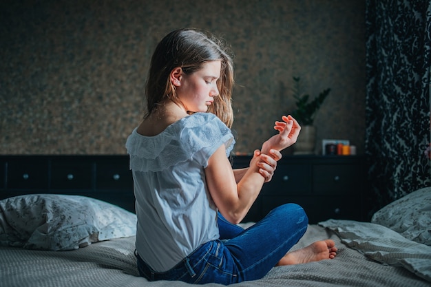 Young dark-haired girl clings to sore wrist while sitting jn bed in her room.