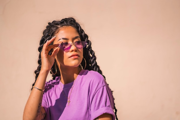 A young dark-skinned woman with purple glasses in an urban session of Latin ethnicity, looking to the right