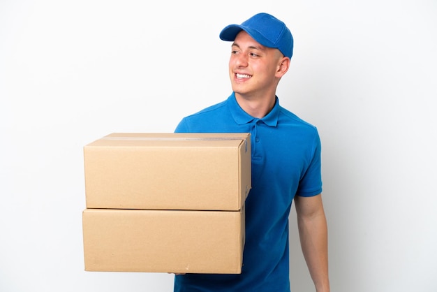 Young delivery Brazilian man isolated ops white background looking to the side and smiling