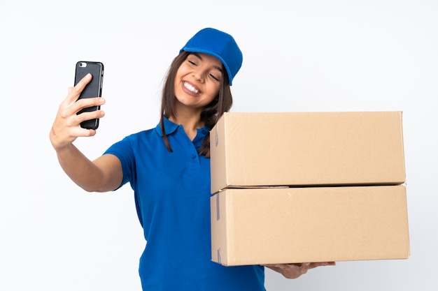 Young delivery brunette woman over isolated white wall making a selfie