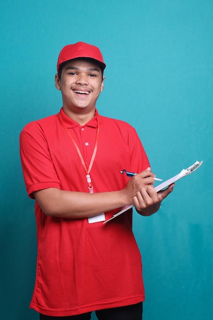 Young delivery man in red uniform checking list on clipboard