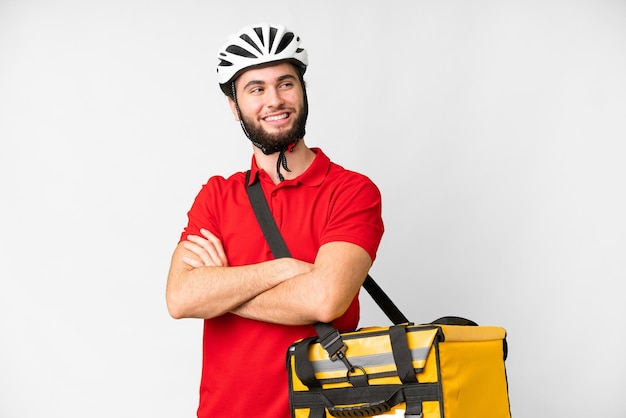 Young delivery man with thermal backpack over isolated white background with arms crossed and happy