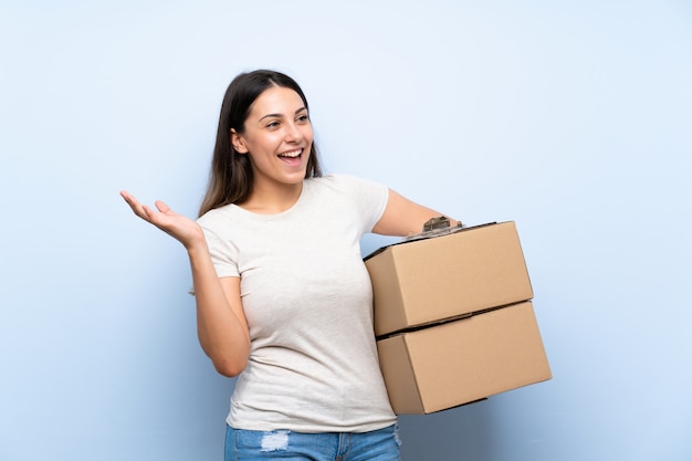 Young delivery woman over blue brick wall with surprise facial expression