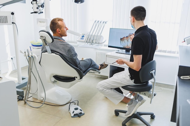 A young dentist doctor tells a male patient about dental care A man was sitting in a dental chair at a doctor's appointment Modern dental treatment