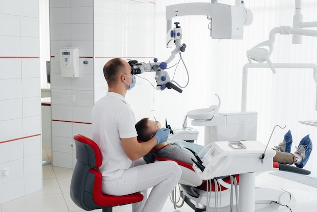 A young dentist examines and treats the teeth of a young guy in modern white dentistry using a microscope Dental prosthetics treatment and teeth whitening Prevention of caries