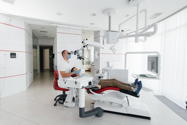 A young dentist examines and treats the teeth of a young guy in modern white dentistry using a microscope Dental prosthetics treatment and teeth whitening Prevention of caries