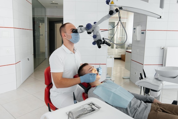 A young dentist examines and treats the teeth of a young guy in modern white dentistry using a microscope Dental prosthetics treatment and teeth whitening Prevention of caries