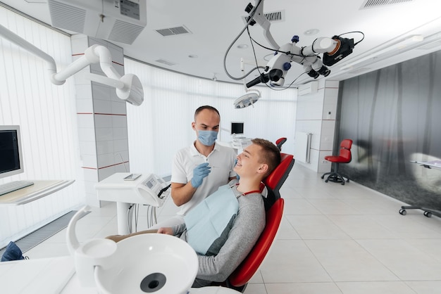 A young dentist examines and treats the teeth of a young man in modern white dentistry closeup Dental prosthetics treatment and teeth whitening Modern dentistry Prevention