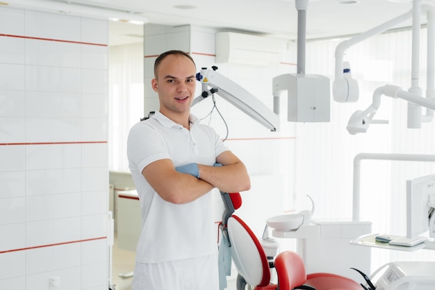 A young dentist stands near a red dental chair and smiles in modern white dentistry Treatment and prevention of caries from youth Modern dentistry and prosthetics