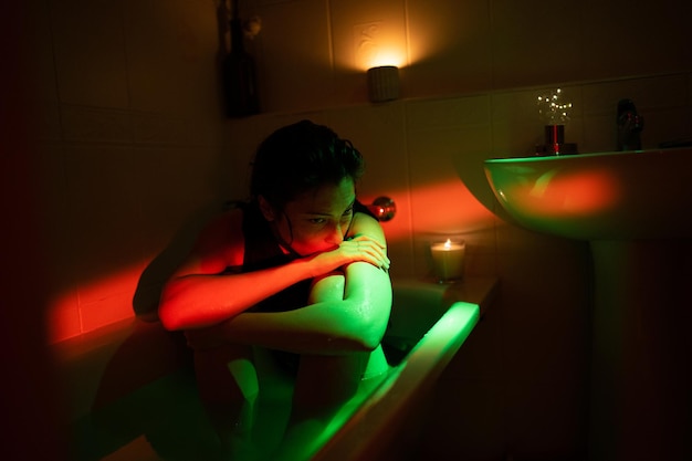 Young depressed lonely woman sitting in bathtub under neon light suffering from breakup depression