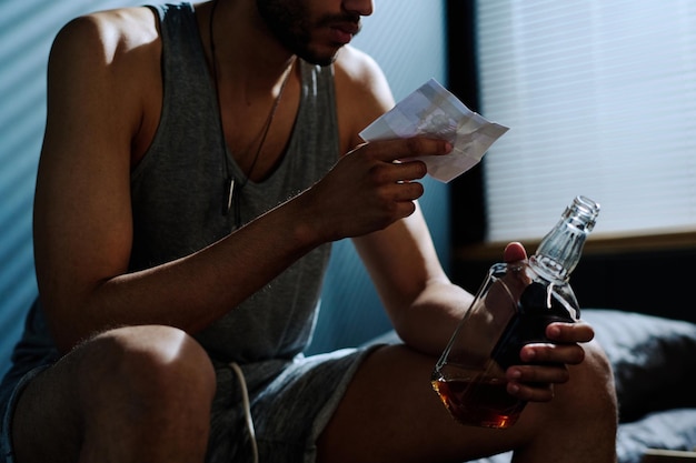 Young depressed man with alcoholic drink looking at picture of him on bike